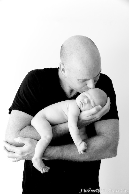 Father kissing newborn sleeping in arms - newborn portrait photography